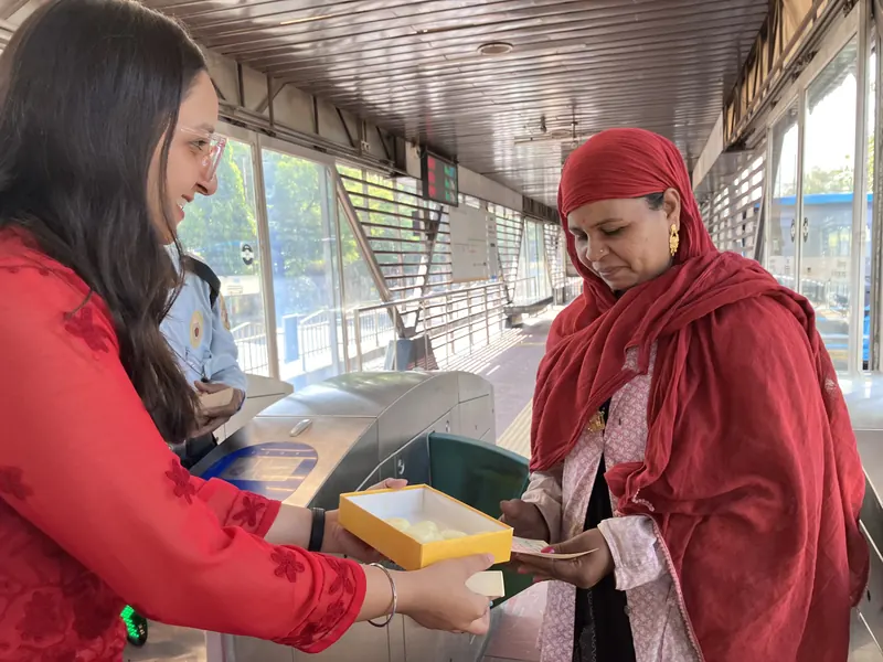 A volunteer offering a box of sweets to a woman at a city bus station in Indore