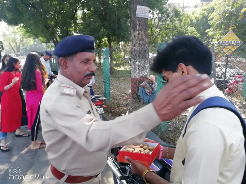 A police constable placing his hand on a young volunteer's head in blessing while the volunteer holds a box of laddoos