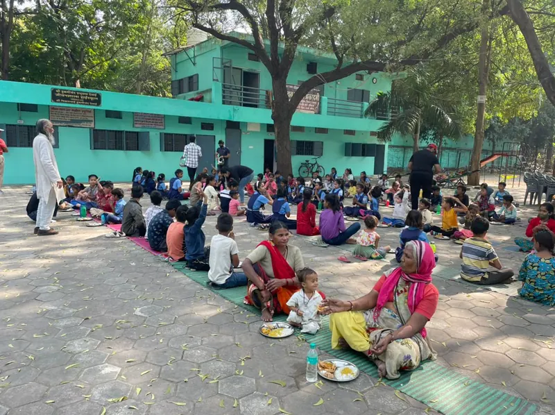 Children seated in rows on mats eating a meal in the school courtyard