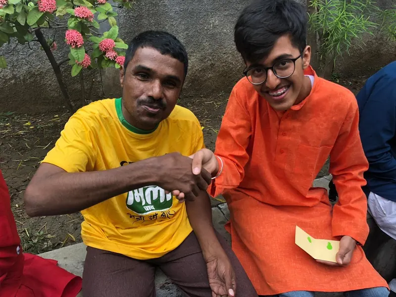 A volunteer in an orange kurta shaking hands with a smiling man in a yellow t-shirt