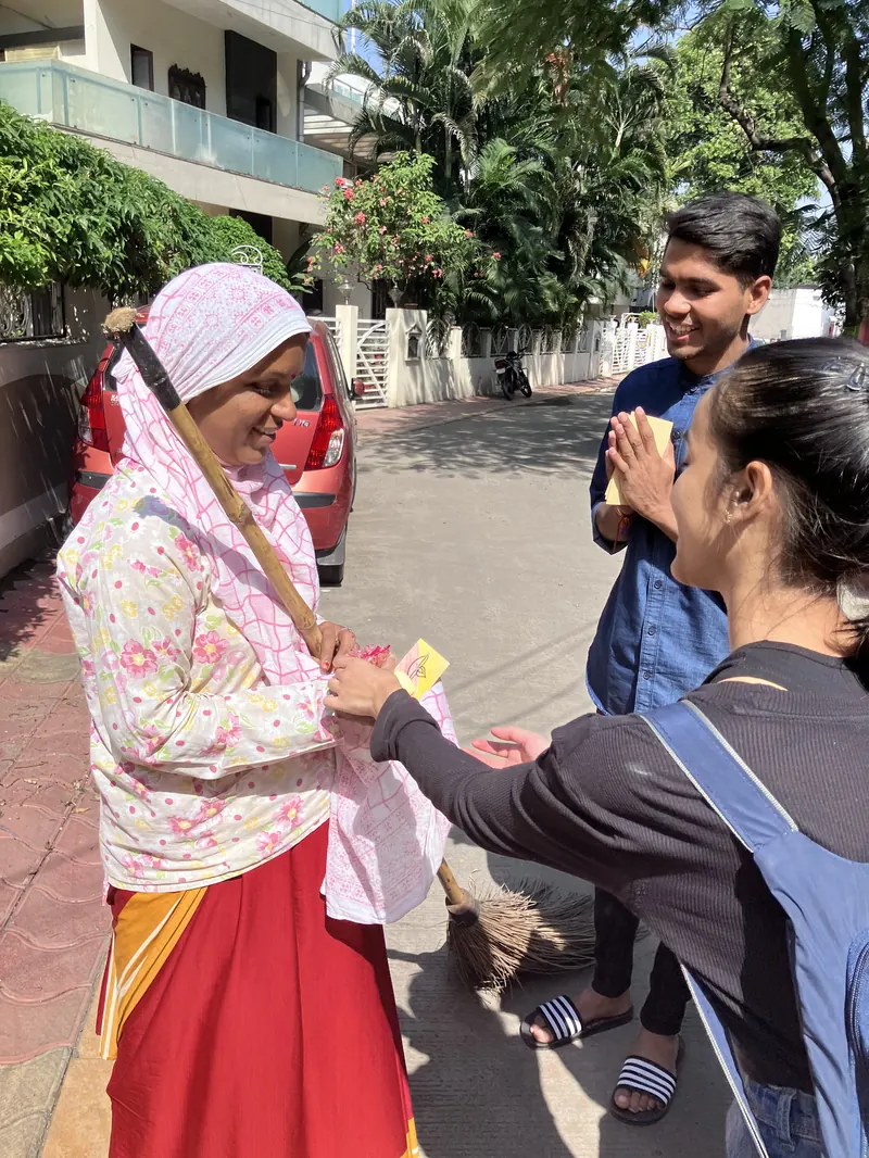 A municipal worker smiling as young volunteers wish her Happy Diwali with folded hands and a handmade card