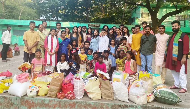 Volunteers and children standing behind rows of donated ration bags at a school in Indore